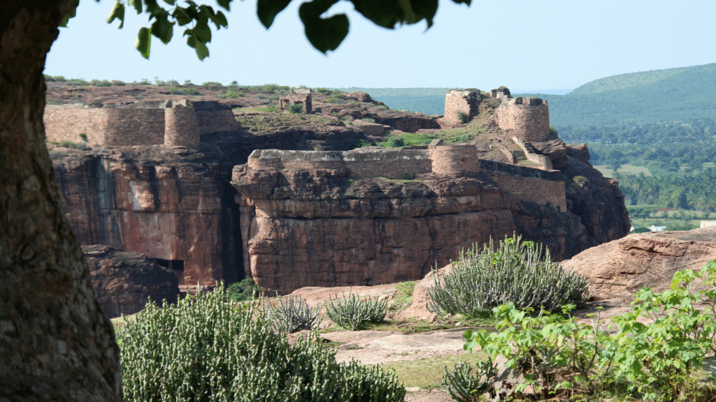 Panoramic view of Badami Fort with sandstone cliffs, Agastya Lake, and heritage sites in the background.